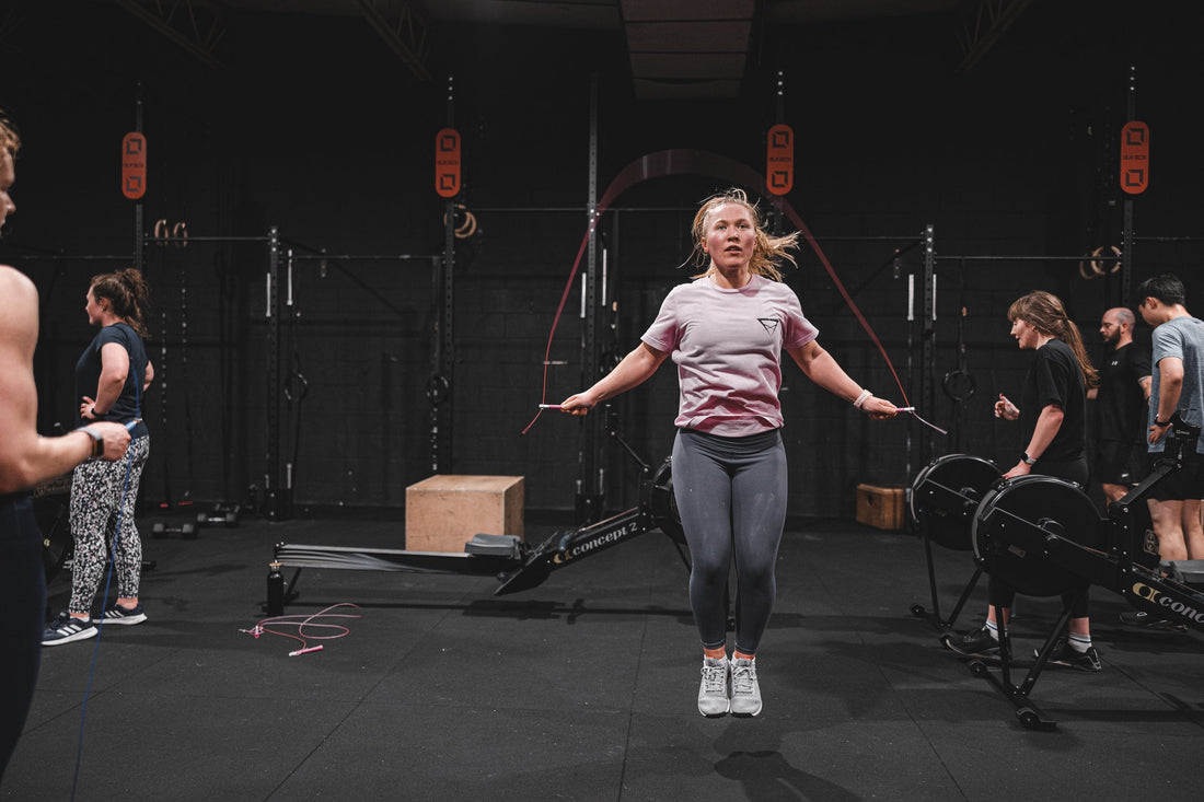 Female athlete skipping rope in a dark functional fitness gym with training equipment behind her