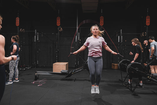 Female athlete skipping rope in a dark functional fitness gym with training equipment behind her