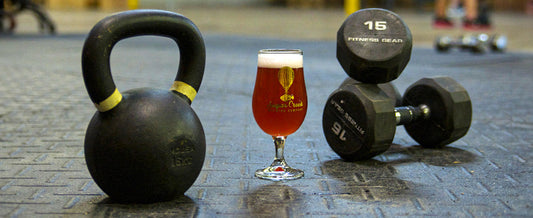 Beer beside kettlebell and dumbbells on a gym floor, illustrating alcohol and post-workout muscle recovery