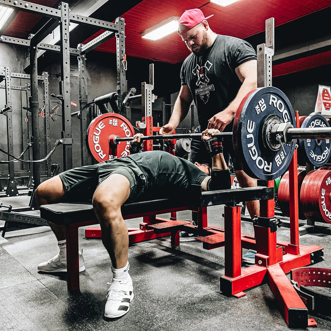 Powerlifter bench pressing a heavily loaded barbell with a spotter in a training gym