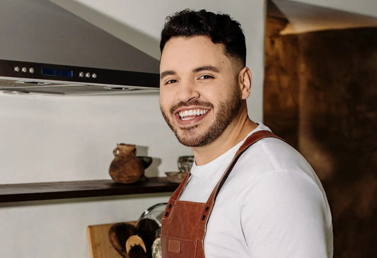 Chef Chris Valdes smiling in a white shirt and brown apron inside a kitchen
