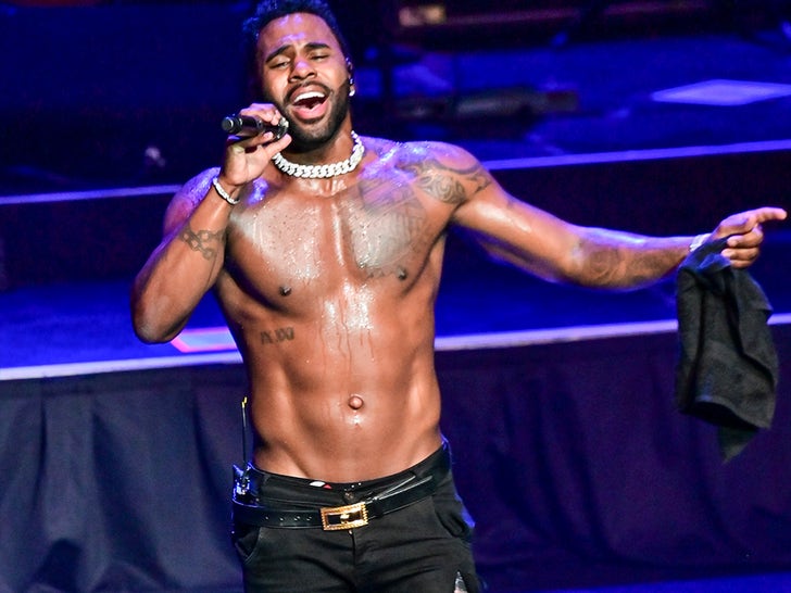 Jason Derulo shirtless onstage singing into a handheld microphone under purple concert lights
