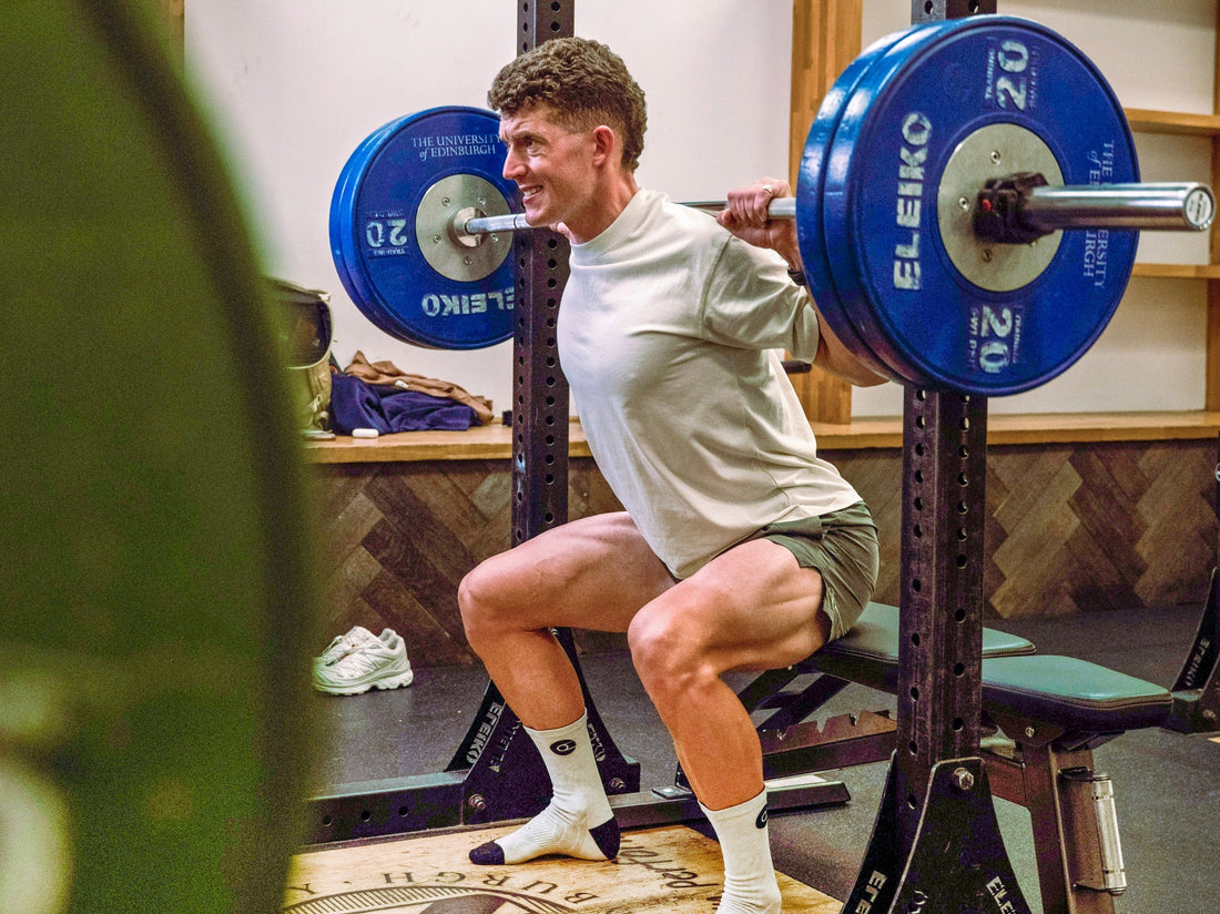 Cyclist performing a barbell back squat in a gym
