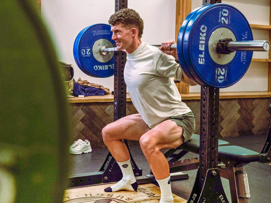 Cyclist performing a barbell back squat in a gym