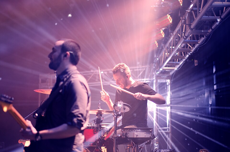 Live rock guitarist and drummer performing under intense stage lights