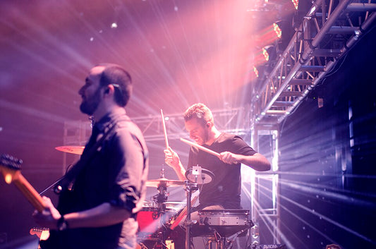 Live rock guitarist and drummer performing under intense stage lights