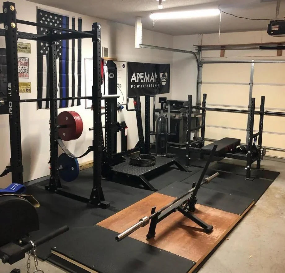 Powerlifting equipment inside a private garage gym with racks, barbells and benches