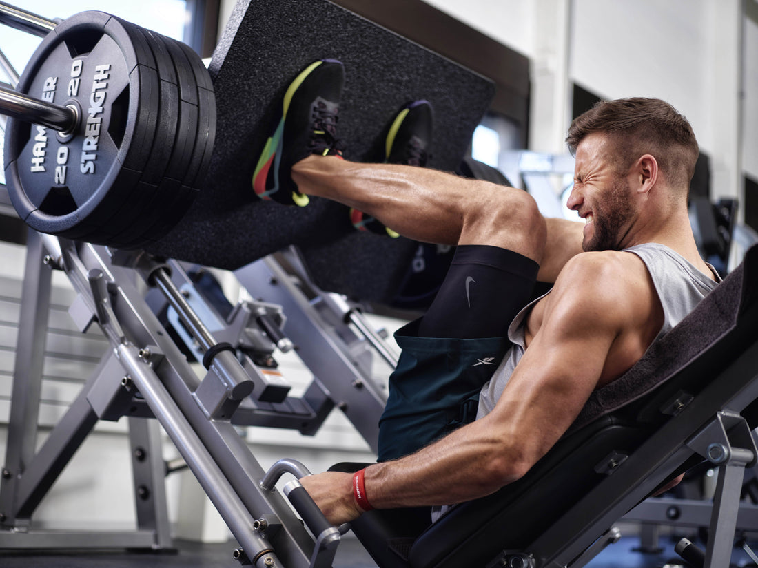 Muscular athlete pressing a loaded leg-press sled in a gym with legs visibly under resistance