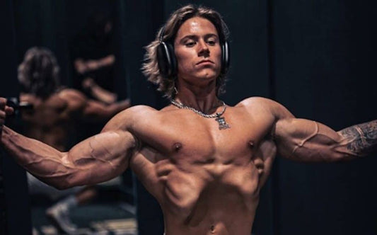 Alex Eubank flexing a lean, muscular upper body in a gym with headphones on