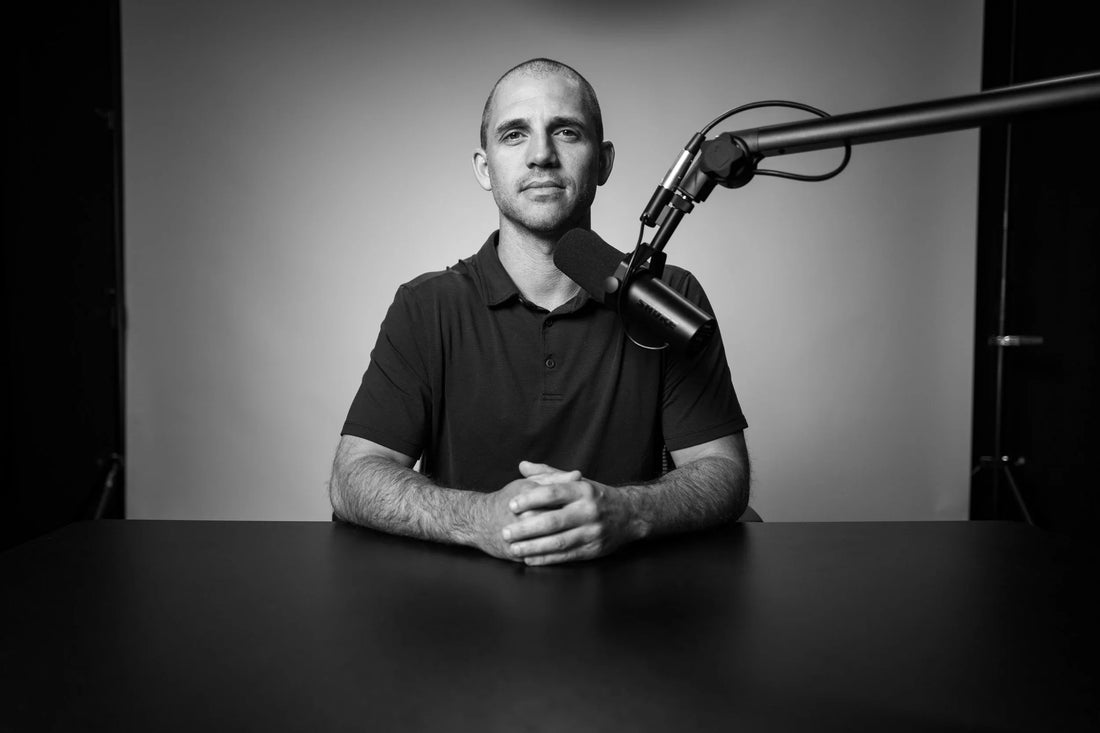 Dr. Andy Galpin seated at a desk with a broadcast microphone in a black-and-white studio portrait.