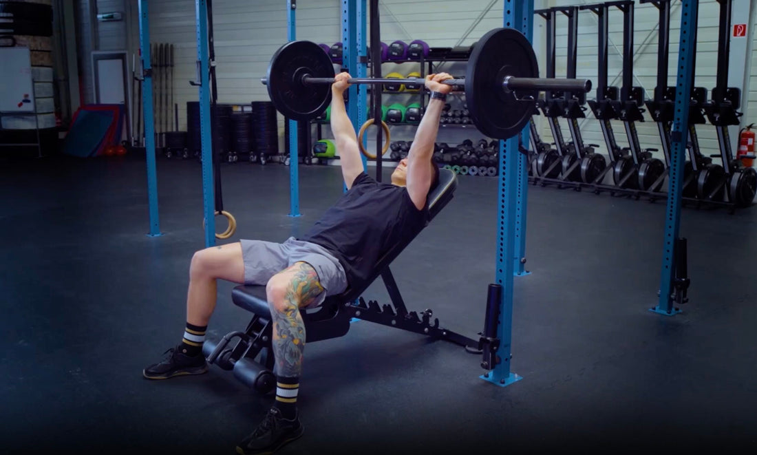 An athlete pressing a loaded barbell on an incline bench in a blue-framed strength gym