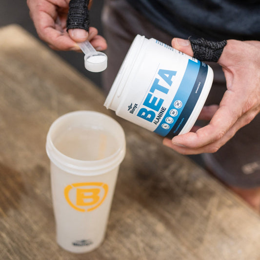 An athlete scooping beta-alanine powder from a supplement tub into a workout shaker bottle