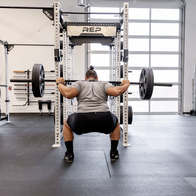 Athlete performing a loaded back squat viewed from behind inside a REP power rack