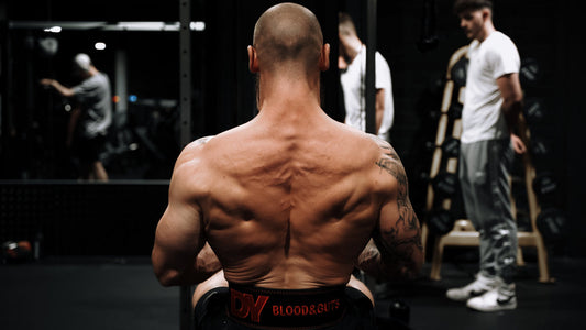 Dorian Yates seated in a gym, his muscular back and Blood and Guts belt visible during a training session
