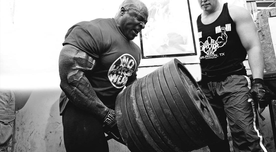 Ronnie Coleman pulling a heavily loaded T-bar row with a spotter in a hardcore gym