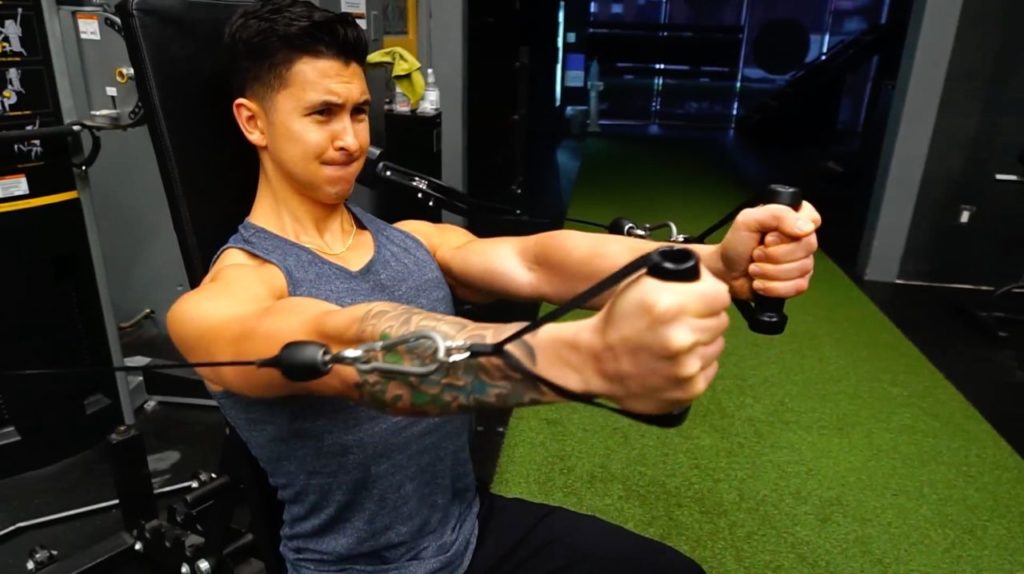 Jeremy Ethier demonstrating a seated cable chest press with both handles in a gym