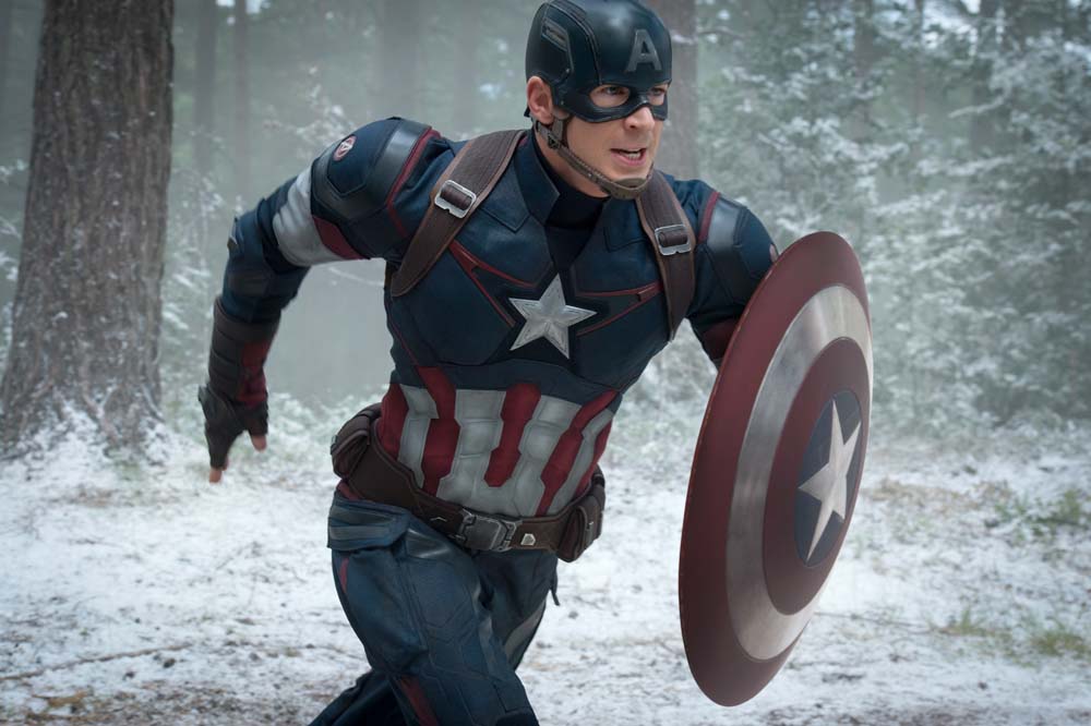 Chris Evans as Captain America in a blue and red tactical suit carrying his shield while running, displaying broad shoulders and an athletic frame