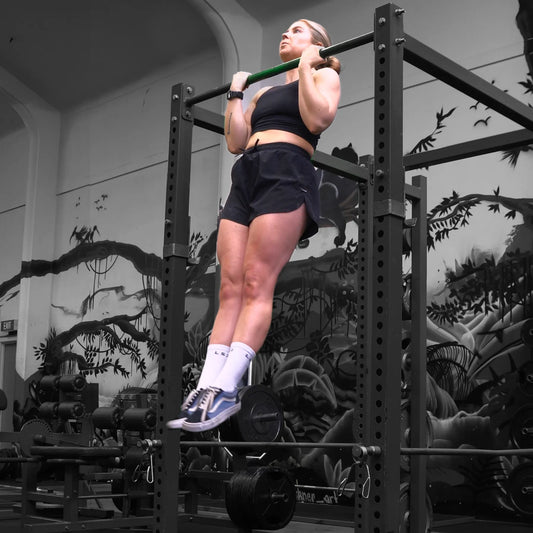 Lance Pecht in a red-and-black sleeveless flannel gripping two balls over a pull-up bar during his July 2026 record attempt