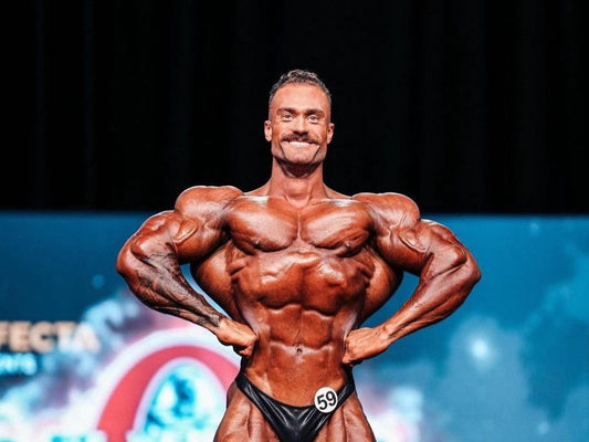 Chris Bumstead posing on the Classic Physique stage with hands on hips and developed shoulders, chest and arms