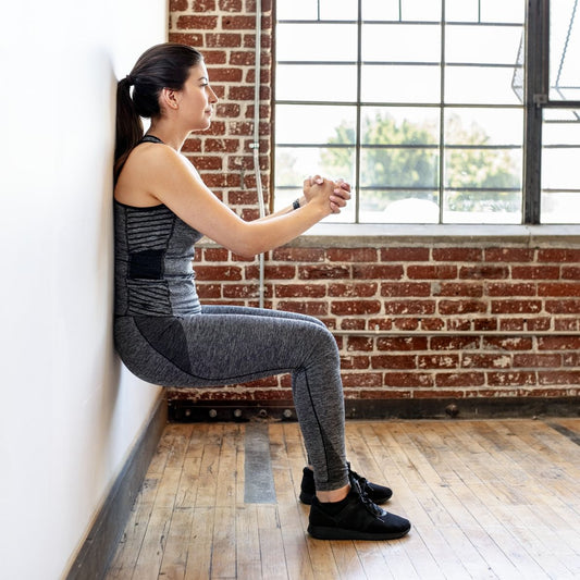 Person performing a controlled wall sit against a gym wall