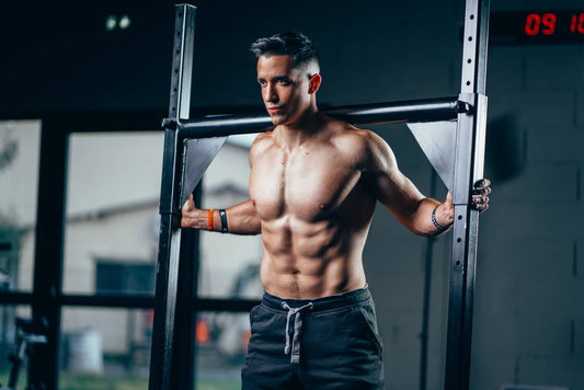Tibo InShape standing shirtless beside a gym rack, showing developed chest and shoulders