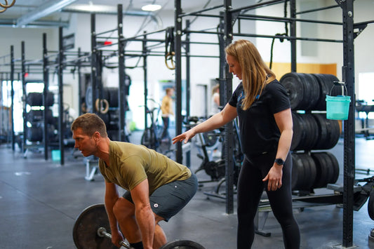 Physical therapist coaching a man through a barbell deadlift in a training gym