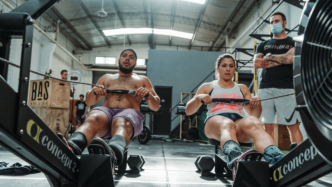 Two athletes rowing side by side on indoor Concept2 rowing machines during CrossFit team training