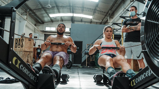 Two athletes rowing side by side on indoor Concept2 rowing machines during CrossFit team training
