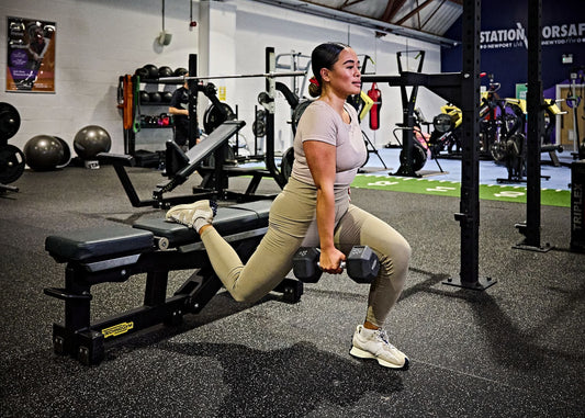 Woman performing a weighted Bulgarian split squat in a gym