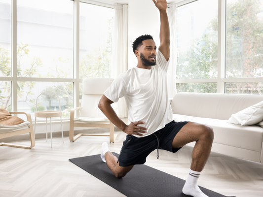 Man performing a half-kneeling hip flexor stretch with one arm overhead in a bright room