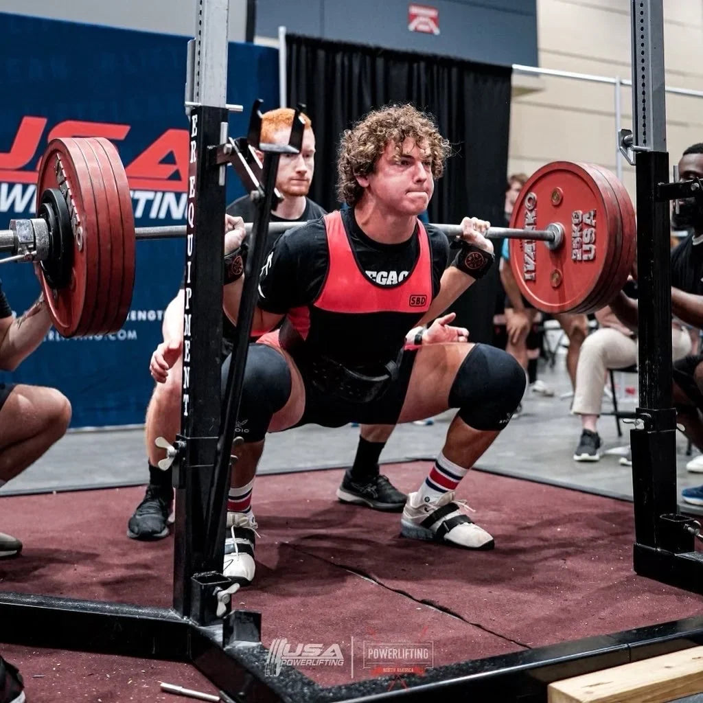 Athlete performing a deep barbell back squat in a powerlifting rack