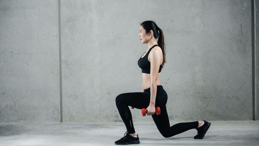 Female athlete performing a controlled dumbbell reverse lunge against a gray wall