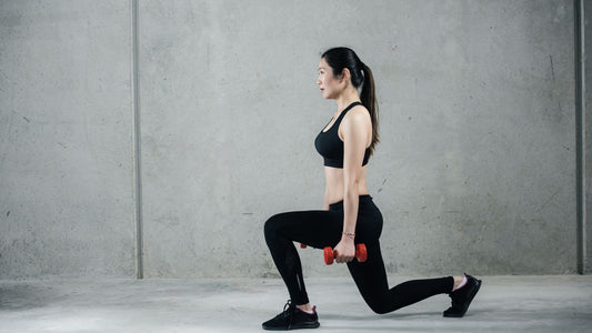 Female athlete performing a controlled dumbbell reverse lunge against a gray wall