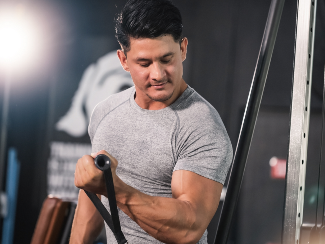 An athlete performing a single-arm Bayesian cable curl with the working arm trailing behind the torso in a gym