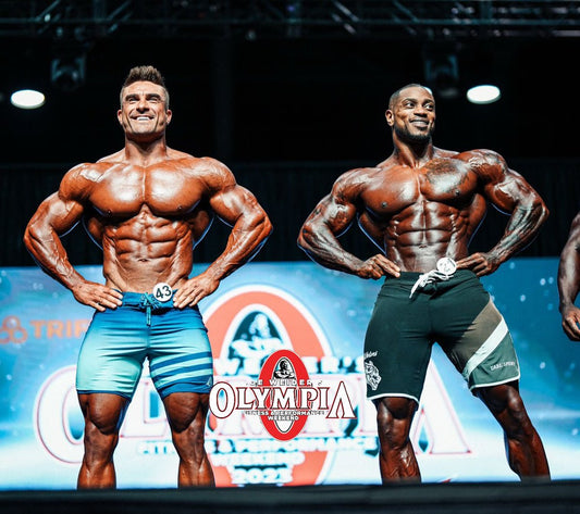 Ryan Terry and Brandon Hendrickson standing side by side in Men’s Physique board shorts on the 2022 Olympia stage