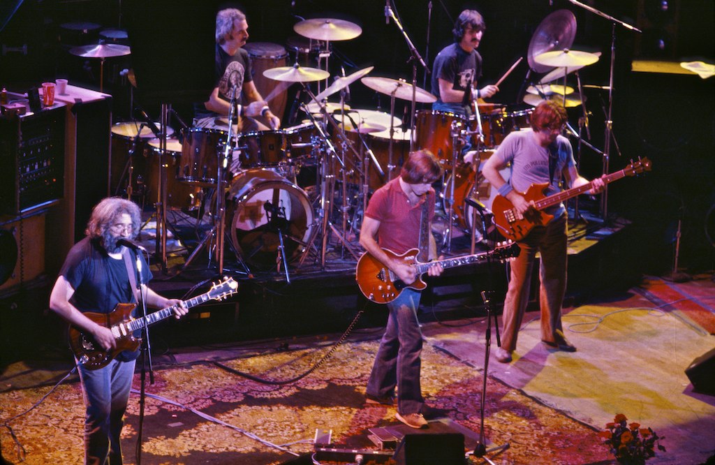 Members of the Grateful Dead playing guitars and drums together onstage at the Warfield Theatre in 1980