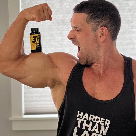 Greg Doucette holding an HTLT 3 Test supplement bottle while flexing his arm