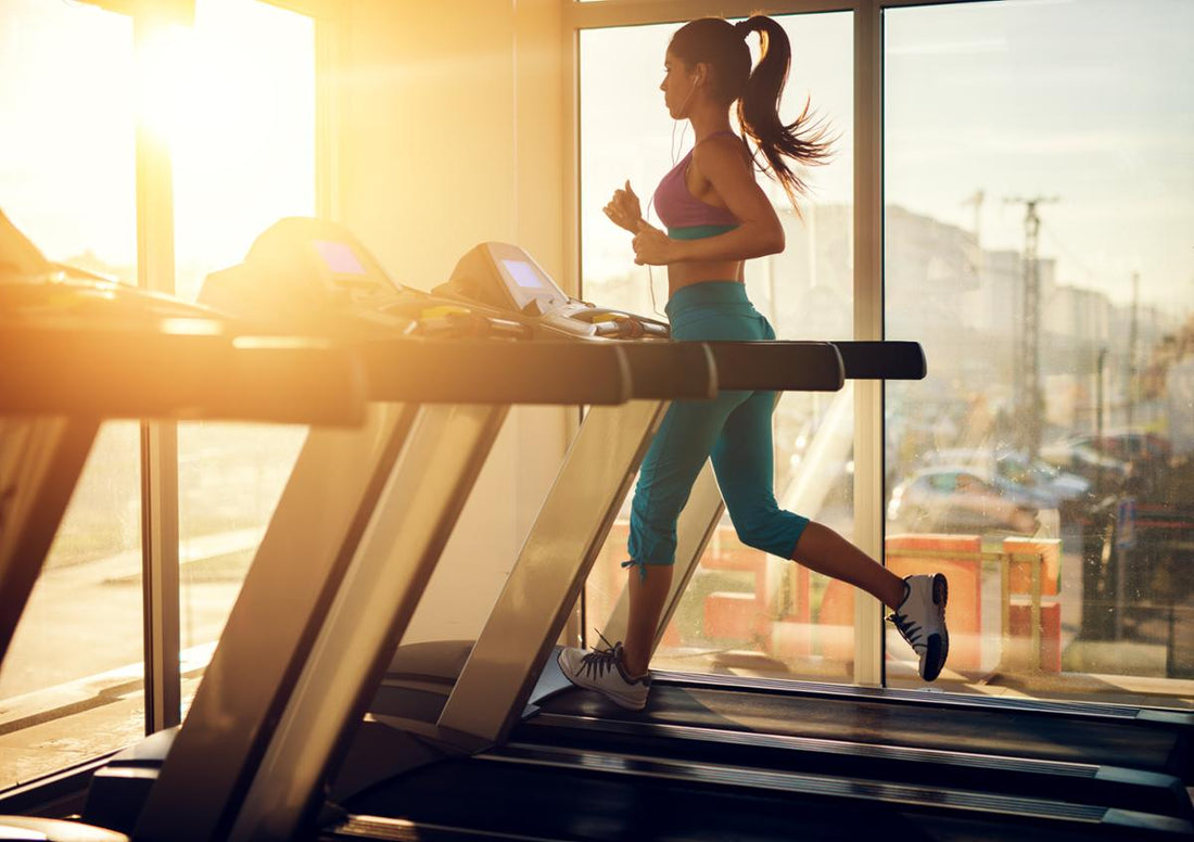 Woman running on a treadmill in warm morning sunlight inside a gym