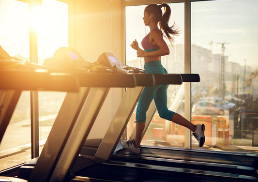 Woman running on a treadmill in warm morning sunlight inside a gym