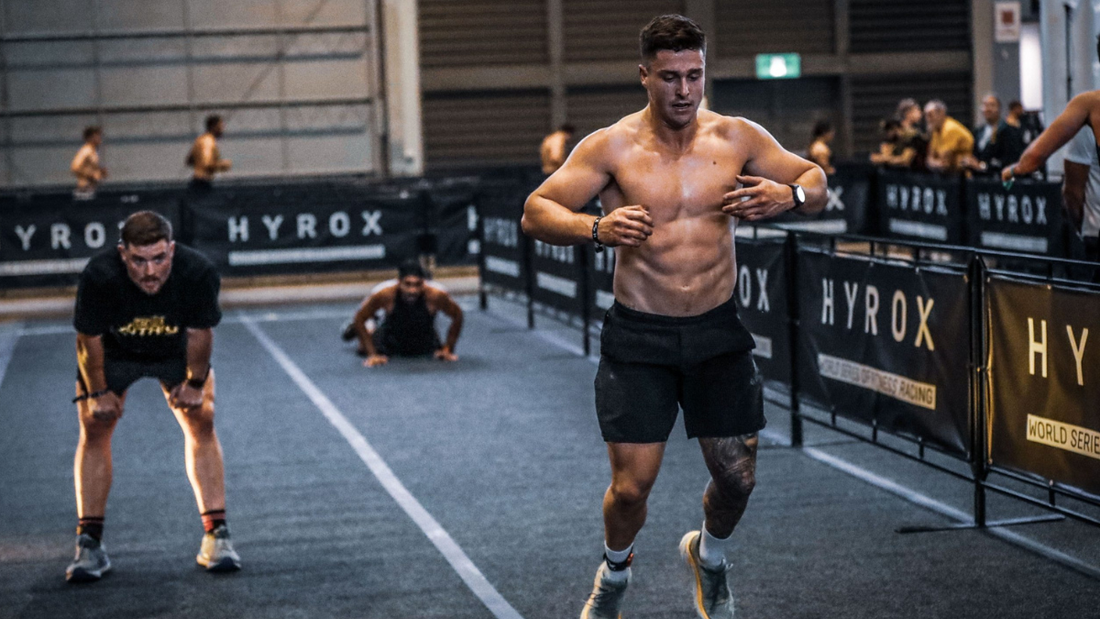 HYROX athlete running on an indoor competition course with other racers and spectators