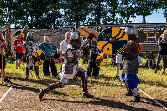 Two armored Viking reenactors facing off with round shields during a staged historical duel