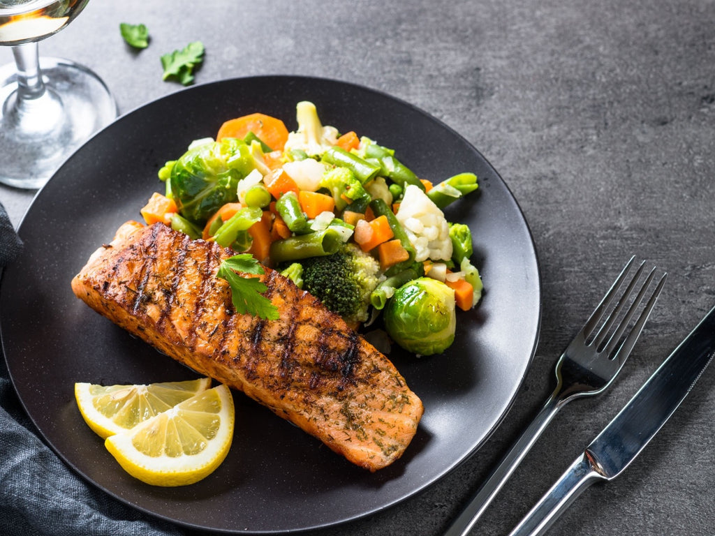 Grilled salmon fillet with vegetables and lemon on a dark plate
