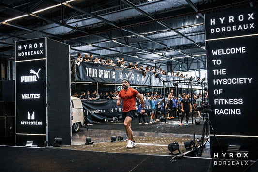 HYROX Bordeaux athlete crossing the finish line in an indoor fitness race