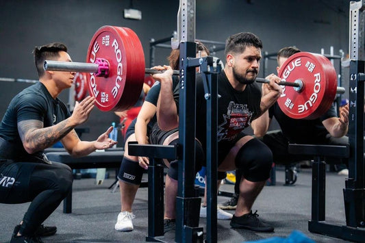 Powerlifter performing a heavy barbell squat with spotters positioned behind the rack
