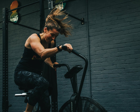 Female athlete pedaling intensely on an air-resistance exercise bike in a functional fitness gym