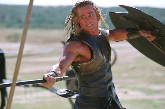 Brad Pitt as Achilles in Troy, wearing bronze armor and thrusting a spear with muscular arms visible