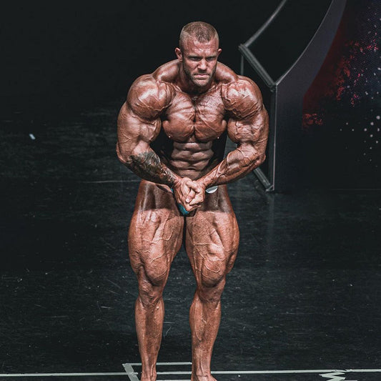 Iain Valliere posing on a bodybuilding stage in green trunks under bright lights