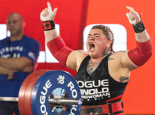 Inez Carrasquillo celebrating a strongwoman victory beside a loaded barbell