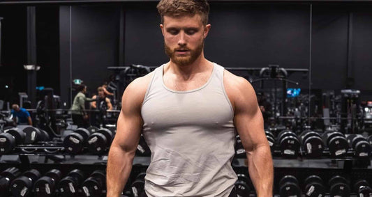 Jeff Nippard standing in a gym wearing a grey tank top, surrounded by free weights