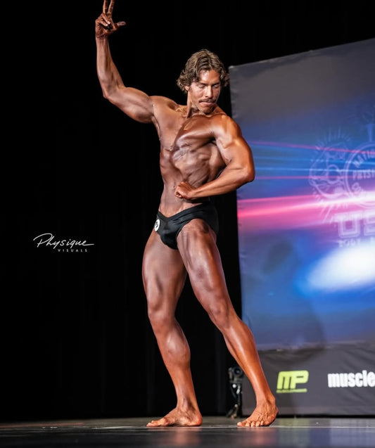 Joseph Baena posing onstage in black trunks at his March 2026 bodybuilding debut